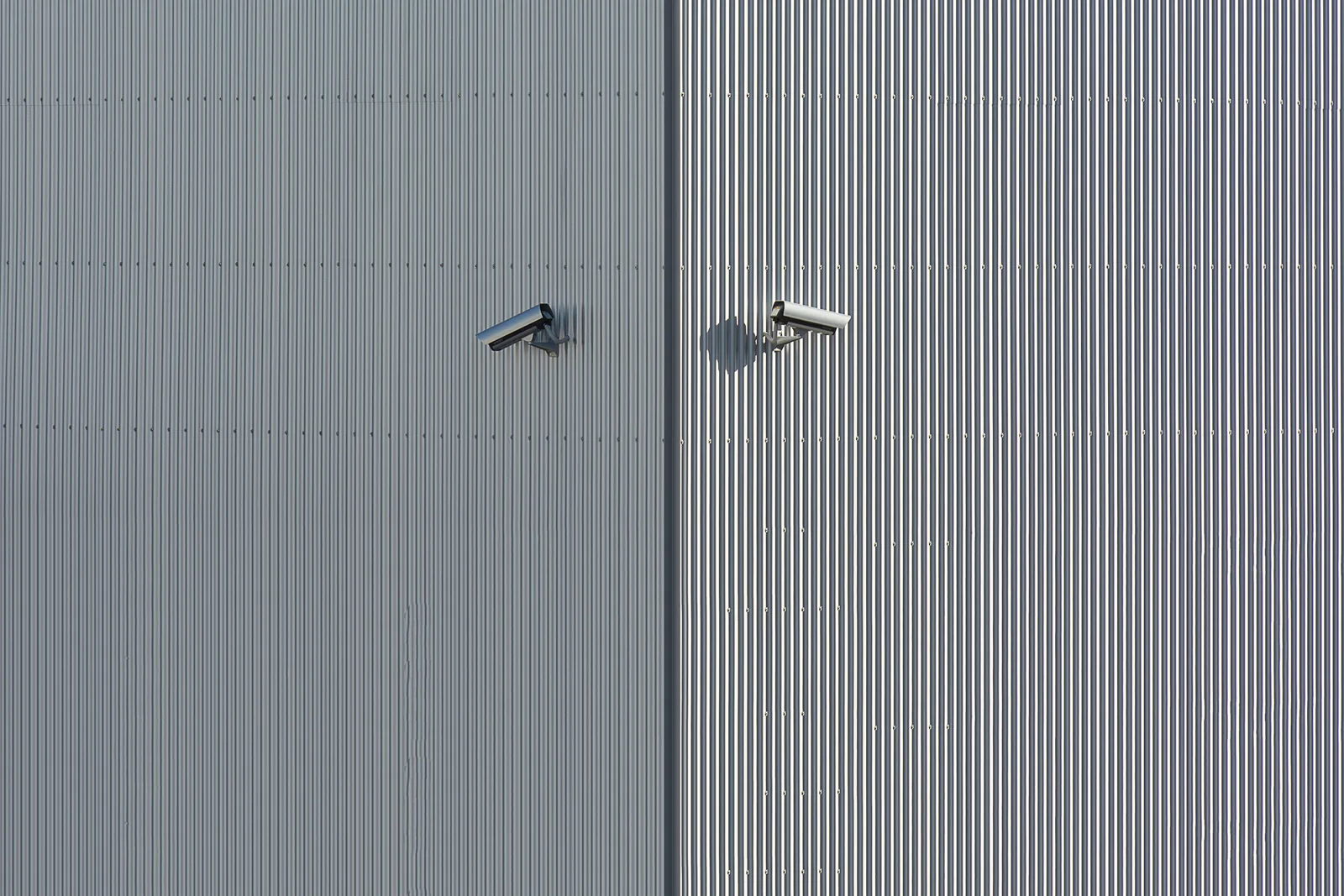 Two bullet security cameras mounted high on a corrugated metal commercial building